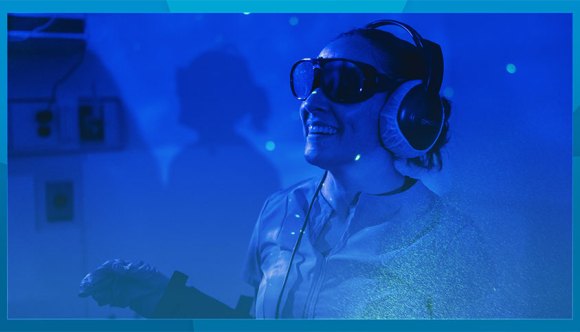 A woman wearing headphones participates in an immersive experience in a dark room.