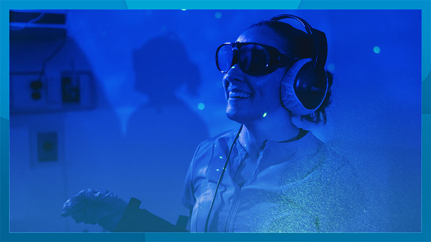 A woman wearing headphones participates in an immersive experience in a dark room.