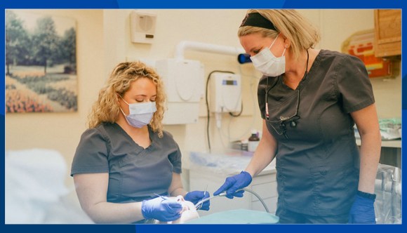 Two dental care providers clean a Veteran’s teeth.