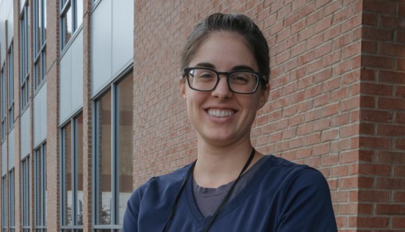 A smiling woman wearing glasses and scrubs outside a VA facility.