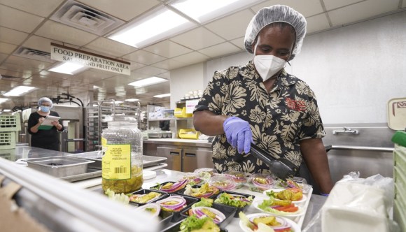 A VA food services worker preps salads for an upcoming meal while a colleague looks on.