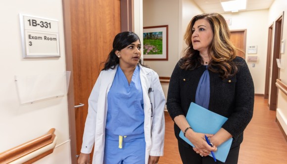 A female gynecologist walks down a hallway with another woman, deep in conversation.