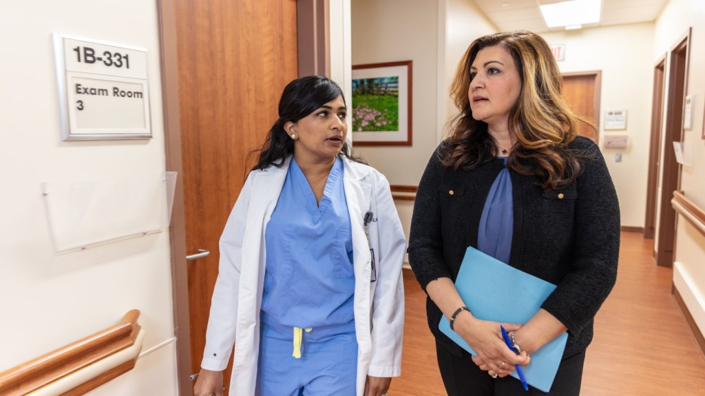 A female gynecologist walks down a hallway with another woman, deep in conversation.