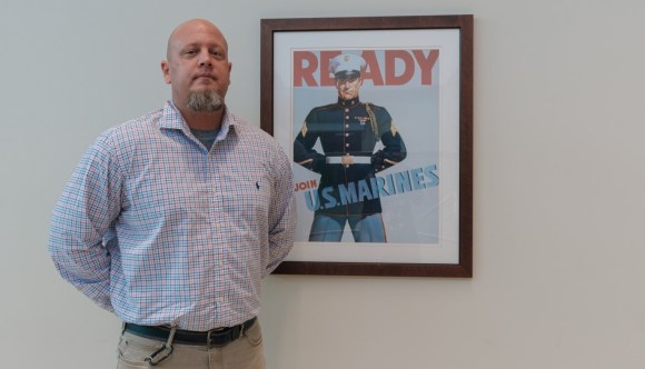 A VA employee, who is also a Veteran, posing next to an antique recruitment poster for the U.S. Marines.