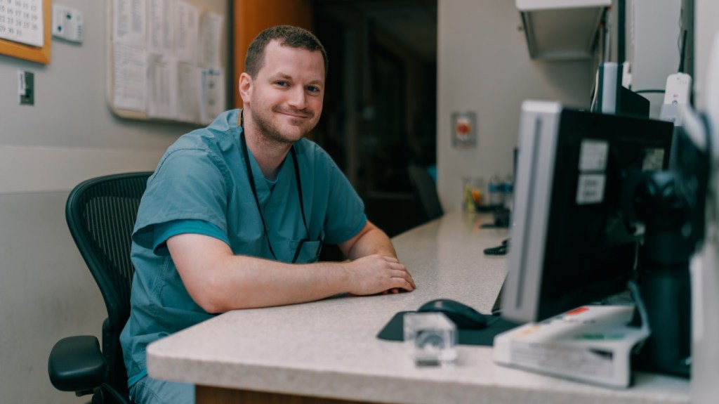 A man in scrubs sits at a computer, enjoying the results of a successful job search that brought him to VA. 