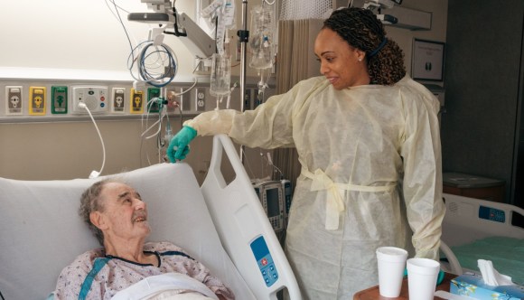 A female nurse assists at the bedside of a Veteran patient.