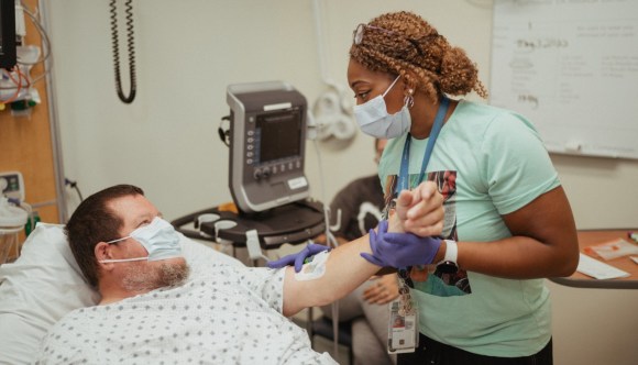 A VA nurse assists a patient with an IV.