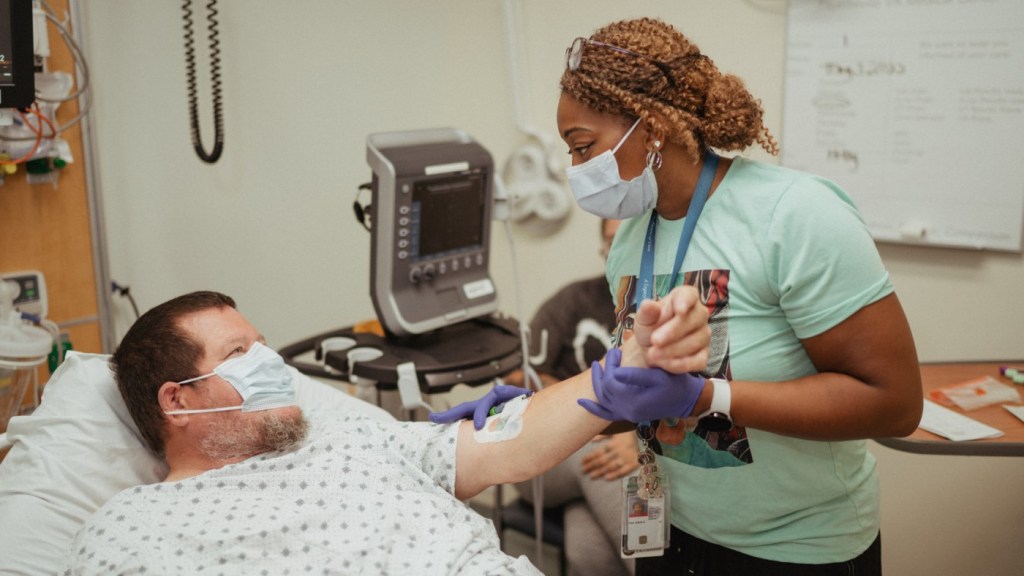 A VA nurse assists a patient with an IV.