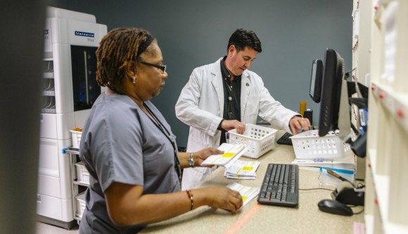 VA pharmacists, working in a pharmacy, surrounded by shelves of medications.