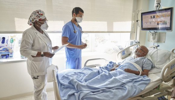 A Veteran patient lies in a hospital bed while two health care professionals provide attentive care. At VA, it’s all about Veterans—ensuring they receive quality medical support.