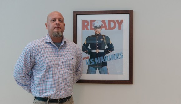 A Veteran VA employee stands next to a reproduction of a vintage U.S. Marines recruitment poster.